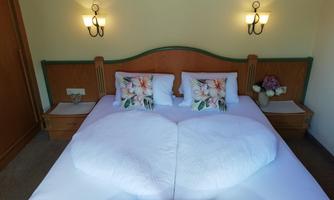 A cozy bedroom with a double bed and decorative pillows. The bedding is folded in a heart shape, and there are nightstands with lamps present.