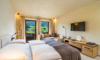 A modern hotel room with two beds and a cozy seating area. Large windows offer a beautiful view of the green landscape.