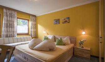 A cozy bedroom with yellow walls and a large bed. The decor is modern and inviting, with a window that lets in daylight.