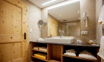 A modern bathroom with wood and stone accents. It features a sink, a mirror, and neatly folded towels.