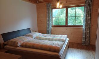 A cozy bedroom with a double bed and wooden paneling. Large windows let in plenty of daylight and offer a view of nature.