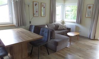 A modern living room with a cozy sofa, a table, and chairs. Large windows provide plenty of daylight and a pleasant atmosphere.