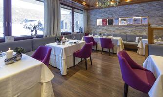 An elegant restaurant with wooden floors and white tablecloths. The tables are set with purple chairs and decorative elements.