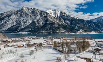 A picturesque winter landscape with snow-covered mountains and a serene lake. Small cottages gently rest in the snowy surroundings.