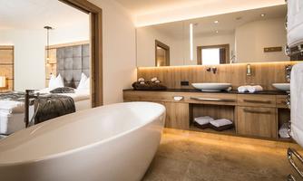 A modern bathroom with a freestanding bathtub and elegant wood design. In the background, a bedroom and a bright, inviting atmosphere are visible.