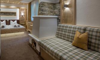 A cozy room with a padded seating area and a wood stove. In the background, two beds and natural materials are visible.