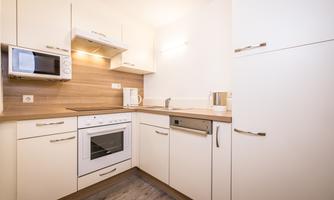 A modern kitchen with white cabinets and wooden details. It is well-equipped with a stove, a microwave, and a refrigerator.