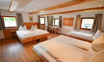 A bright, cozy room with three beds and wooden details. There are windows with a view outside and a small table.