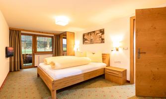 A cozy hotel room with a double bed and wooden furniture. Large windows provide plenty of natural light and a view outside.