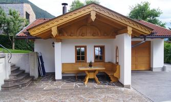 A cozy wooden house with a traditional roof. In front of the house, there is a seating area with a table.