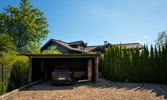 A modern house with a carport and a car in the driveway. Surrounded by trees and green bushes, the scene exudes tranquility and elegance.