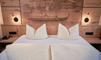 A cozy bedroom with a large bed and two decorative pillows. The warm wood paneling and soft lighting create an inviting atmosphere.