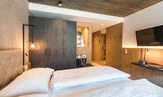 A modern bedroom with a large bed and stylish furniture. There is a simple decor and an adjoining bathroom.