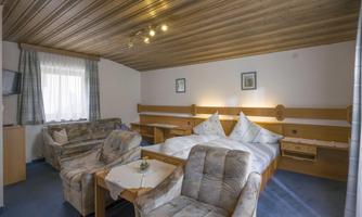 A cozy hotel room with two beds and comfortable armchairs. The wooden ceiling and soft colors create a relaxed atmosphere.