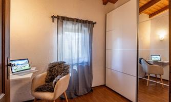A small workspace with a desk, a chair, and two monitors. The walls are light, and there is a window with a curtain.