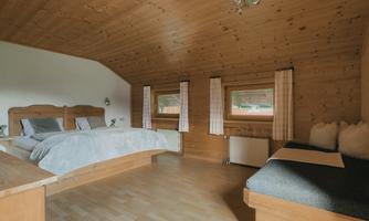A cozy bedroom with wooden ceilings and a large bed. The windows let in natural light and offer a view of the outdoors.
