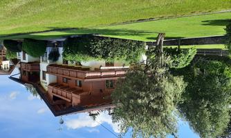 A beautiful, traditional wooden house with balconies and a well-kept garden. Surrounded by lush greenery and trees under a blue sky.