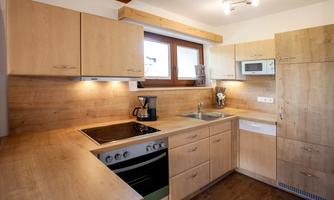 A modern kitchen with wooden cabinets and a bright countertop. It is equipped with a stove, a microwave, and a small sink.