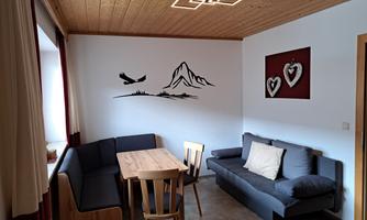 A cozy living space with a wooden table and chairs. On the wall, there is a mountain motif as well as two decorative hearts.