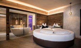A stylish bedroom with a round bed and modern wood design. The room features a connection to an elegant bathroom.