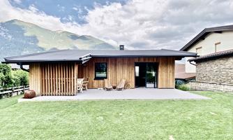 A modern wooden house with a terrace and a view of the mountains. The well-kept lawn and the surrounding landscape create an inviting atmosphere.