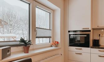 A modern kitchen with white cabinets and an oven. Through the windows, you can see a snow-covered landscape.