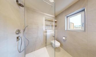 A modern shower with glass partition in a bright bathroom. There is also a window and shelves for toiletries.
