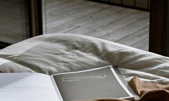 A cozy bed with a blanket and an open book. The room has a calm, relaxed atmosphere.