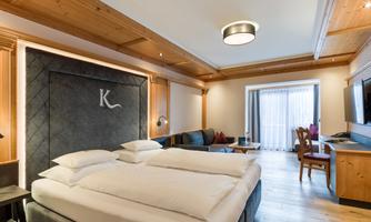 A modern hotel room with two single beds and wooden ceilings. There is a cozy seating area and plenty of daylight.