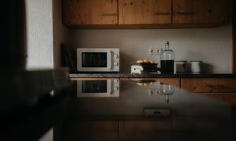 A modern kitchen with wooden cabinets and a clear, simple design. On the countertop, there is a microwave, as well as some additional kitchen utensils.