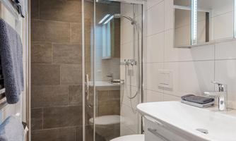 A modern bathroom with a glass shower cubicle and an elegant sink. The walls are tiled in light colors, and large tiles create a contemporary look.