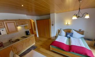 A cozy room with wood decor, a double bed, and a kitchenette. The space features bright colors and an inviting atmosphere.