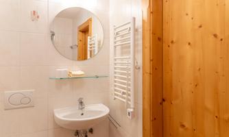 A modern bathroom with a round mirror and a sink. The walls are brightly tiled, and a wooden partition adds warmth.