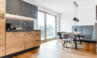 Modern kitchen with wooden cabinets and a dining table. Large window area with plenty of natural light.