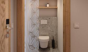A modern toilet with a gray floor and an elegant wall covering. There are wooden shelves and soft lighting.