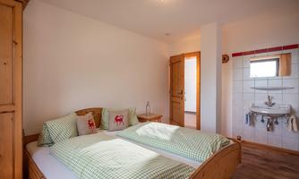 A bright room with two single beds and checkered bed linen. In the background, there is a small sink and a window.