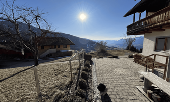 A picturesque mountain landscape with sunshine and a clear blue sky. In the foreground, you can see a cobblestone path and cozy houses.