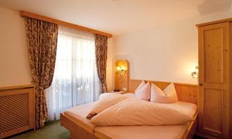 A cozy bedroom with a double bed and wooden paneling. The windows are decorated with curtains, and plenty of daylight floods in.