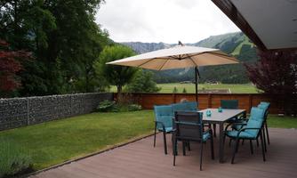 An inviting outdoor area with a table and chairs under a large umbrella. In the background, green hills and trees can be seen.