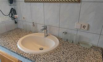 A bathroom with a large sink on a granite surface. The mirror above the sink reflects the space.