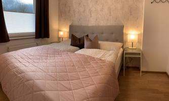A cozy bedroom with a large bed and pink bedding. Two nightstands with lamps are on both sides of the bed.