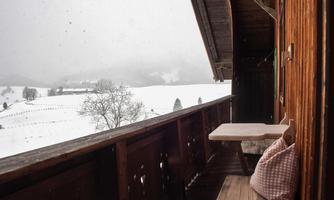 A balcony with wooden cladding and seating. In the background, a snowy landscape is visible under a gray sky.