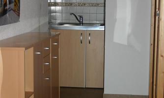 A simple kitchen with wooden cabinets and a small sink. The room has a bright, neutral atmosphere.