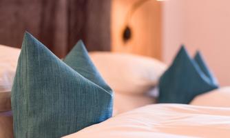 A cozy bedroom with two beds and stylish triangular pillows in blue. The soft lighting creates a relaxed atmosphere.