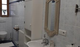 A modern bathroom with white tiles and blue accents. There is a sink, a mirror, and a toilet.