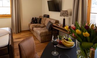 A cozy living space with a couch, a TV, and a table. On the table are wine, glasses, and fresh flowers.