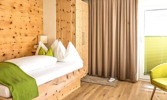 A modern room with wooden paneling and a simple design. It features a bed, a wardrobe, and large windows with curtains.