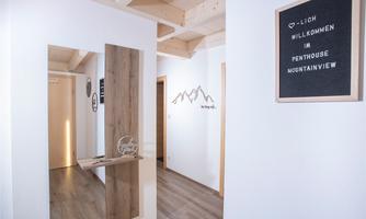 An elegant hallway with wooden details and a mirror. A welcome sign for the penthouse "Mountain View" is hanging on the wall.