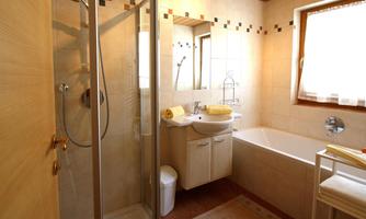 A bright bathroom with a shower and a bathtub. There is a wash area with a mirror and some towels.
