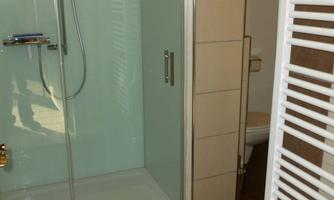 A modern bathroom with a glass shower cubicle. A towel is on the floor and a heater is mounted on the wall.